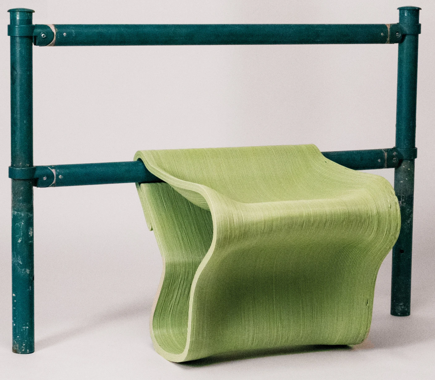 A Morari Stool in Green attatched to a bus stop railing