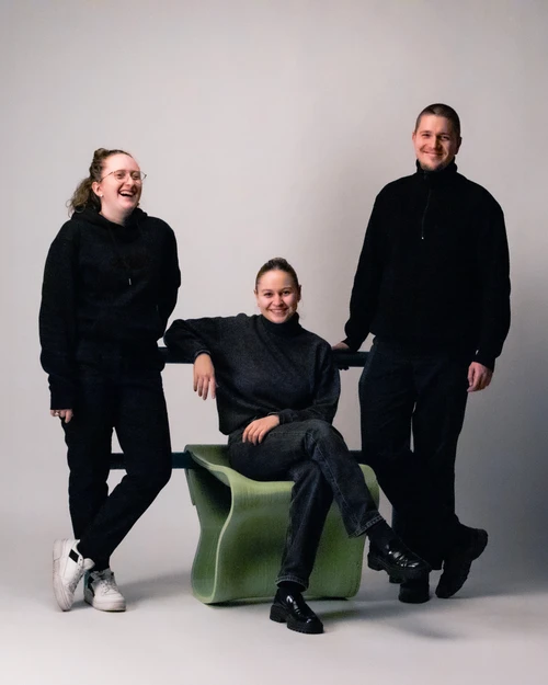 Porträt der drei Designer:innen Valentina Lenk, Klara Schneider und Jesse Altmann. Valentina lacht und Klara und Jesse lächeln. Klara sitzt auf einem Morari Stool.
